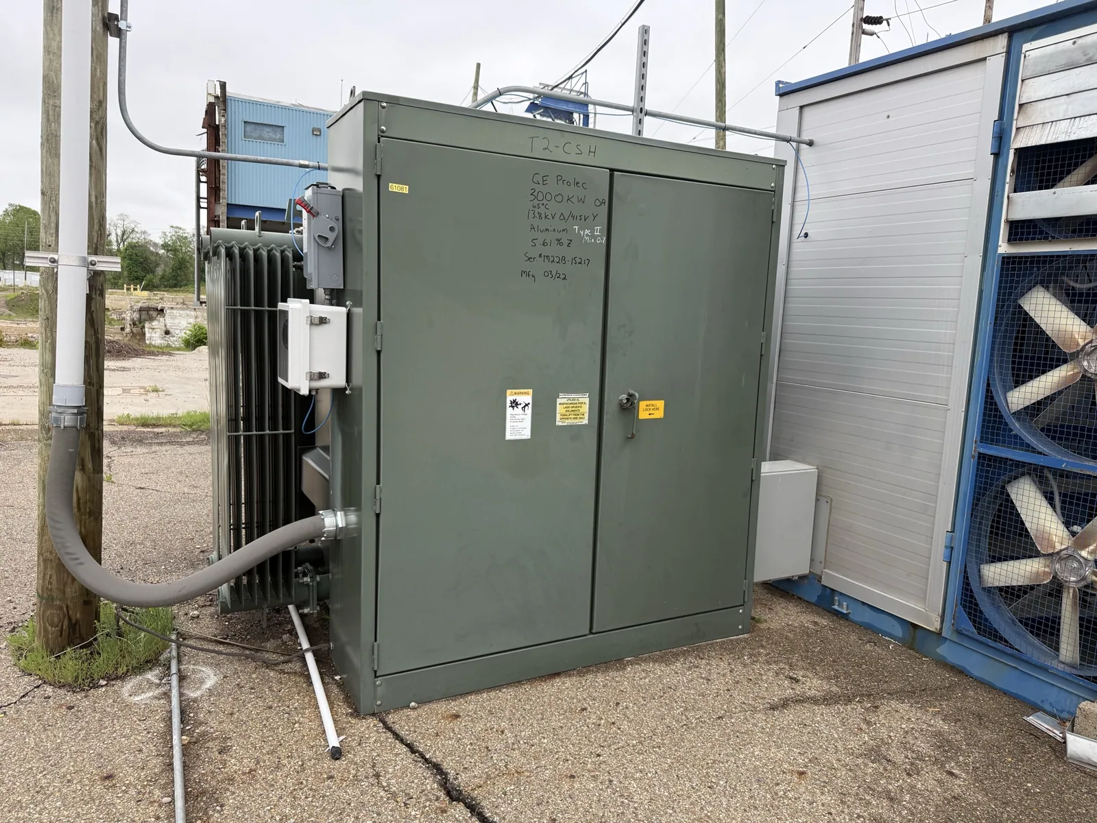 Green pad-mount transformer with radiator fins beside a plant building — Flint, MI